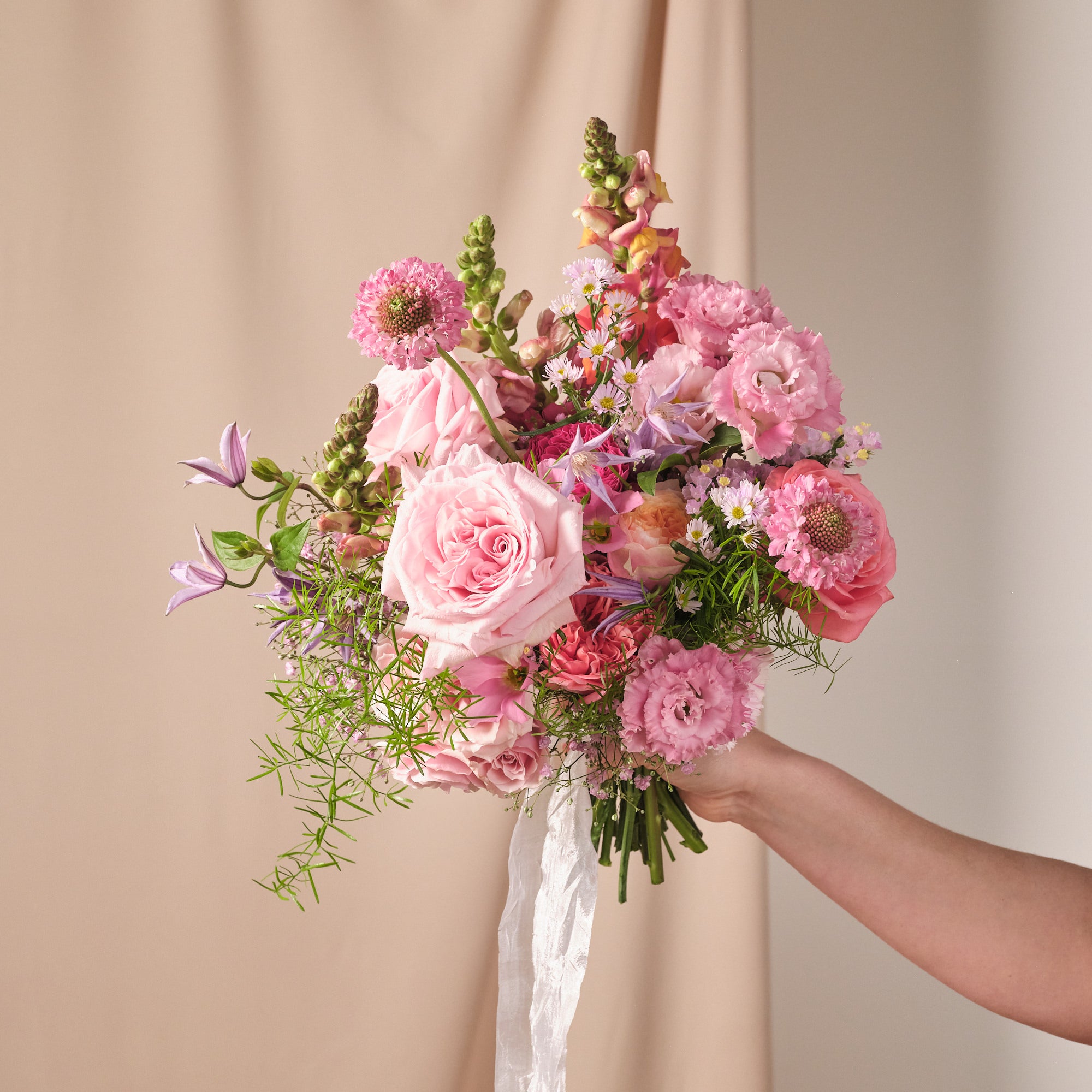 A bridal bouquet with vibrant pink, coral, and soft lilac flowers, arranged naturally and tied with a silk ribbon.